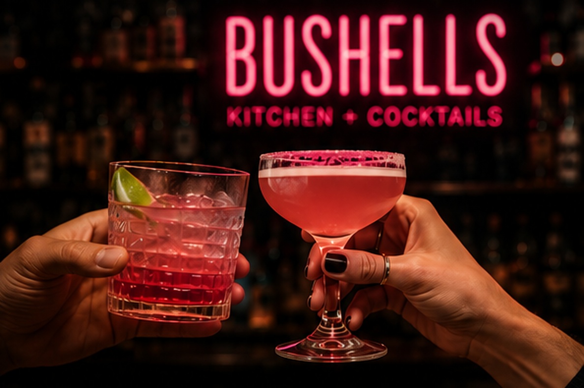 Two hands toasting cocktails under the neon Bushell's sign